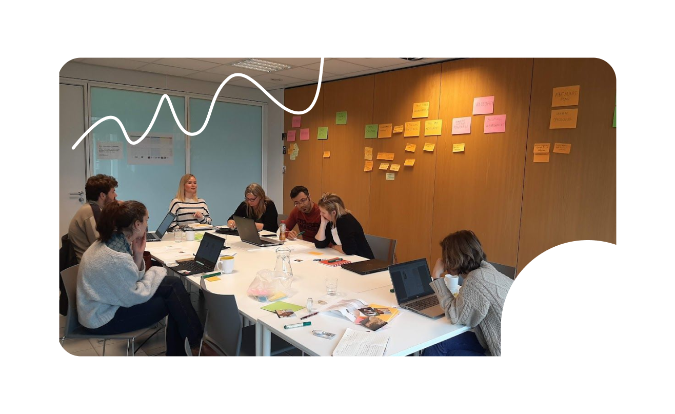 Foto van mensen rond een tafel en post-it's aan de muur